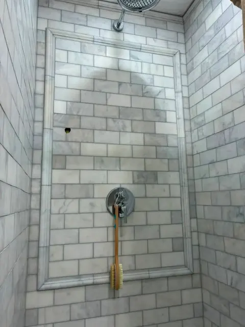 Shower wall of white marble subway tile with a large framed feature panel of the same tile around the valve