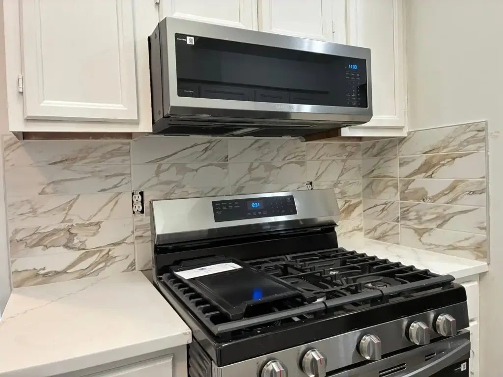 Marble-look slab backsplash with grey and gold veins behind a stainless gas range and microwave