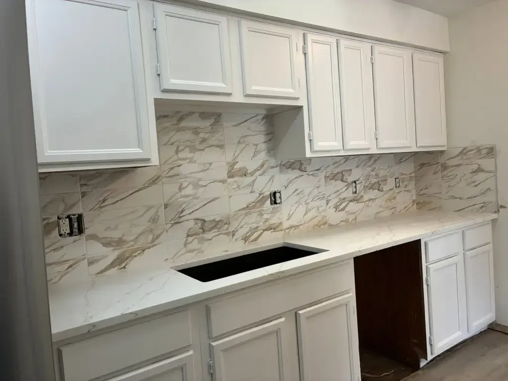 White kitchen cabinets over a white counter with a marble-look tile backsplash