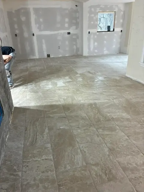 Open room with a new large-format stone-look tile floor, walls still bare drywall
