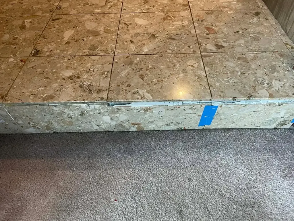 Large stone-look tiles wrapped over the edge of a raised platform, held with blue tape while they set