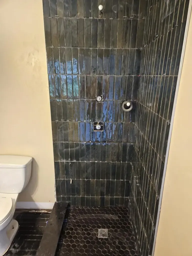 Shower of dark blue-green glazed tiles stacked vertically, with a black hexagon mosaic floor