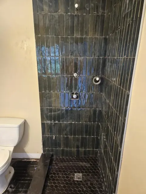Shower of dark blue-green glazed tiles stacked vertically, with a black hexagon mosaic floor