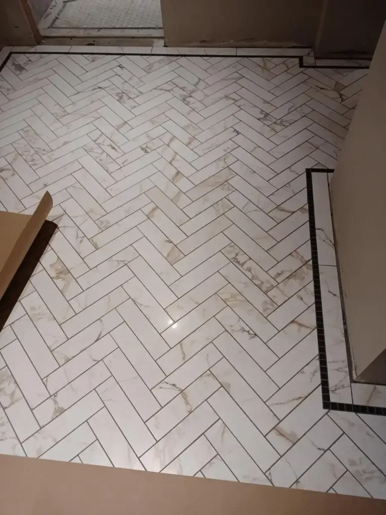 White tile floor laid in herringbone inside a thin black tile border