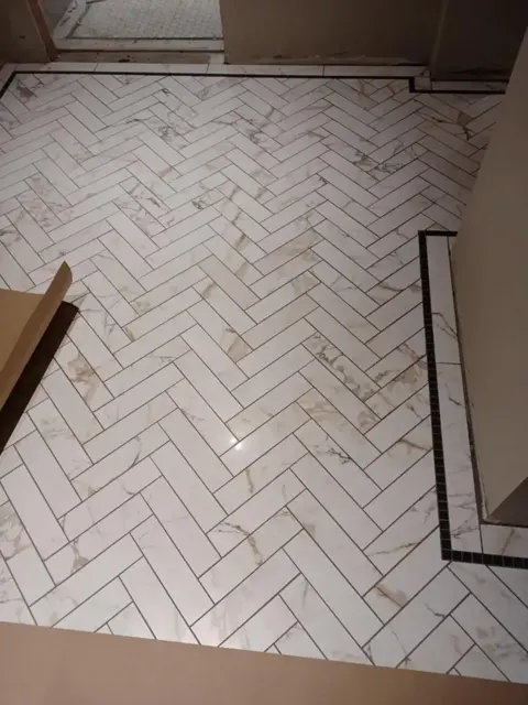White tile floor laid in herringbone inside a thin black tile border