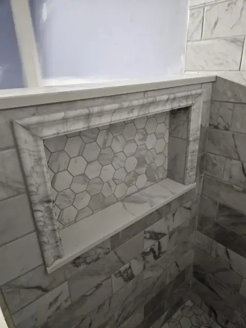Shower niche lined with small marble hexagon mosaic, framed all round by a marble picture-frame trim in a marble-look wall
