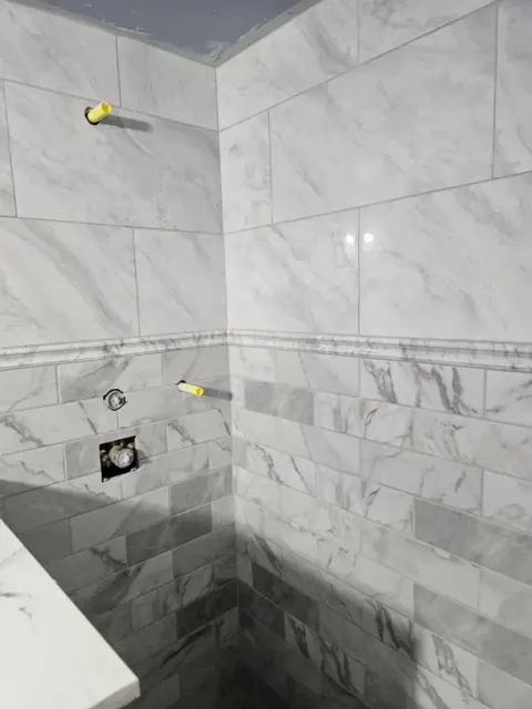 Shower walls with large marble-look tiles above, marble subway tile below and a thin pencil liner between them