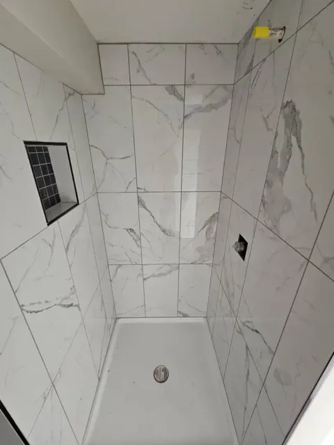 Walk-in shower with large marble-look wall tiles, a niche lined in small black tiles and a white shower base