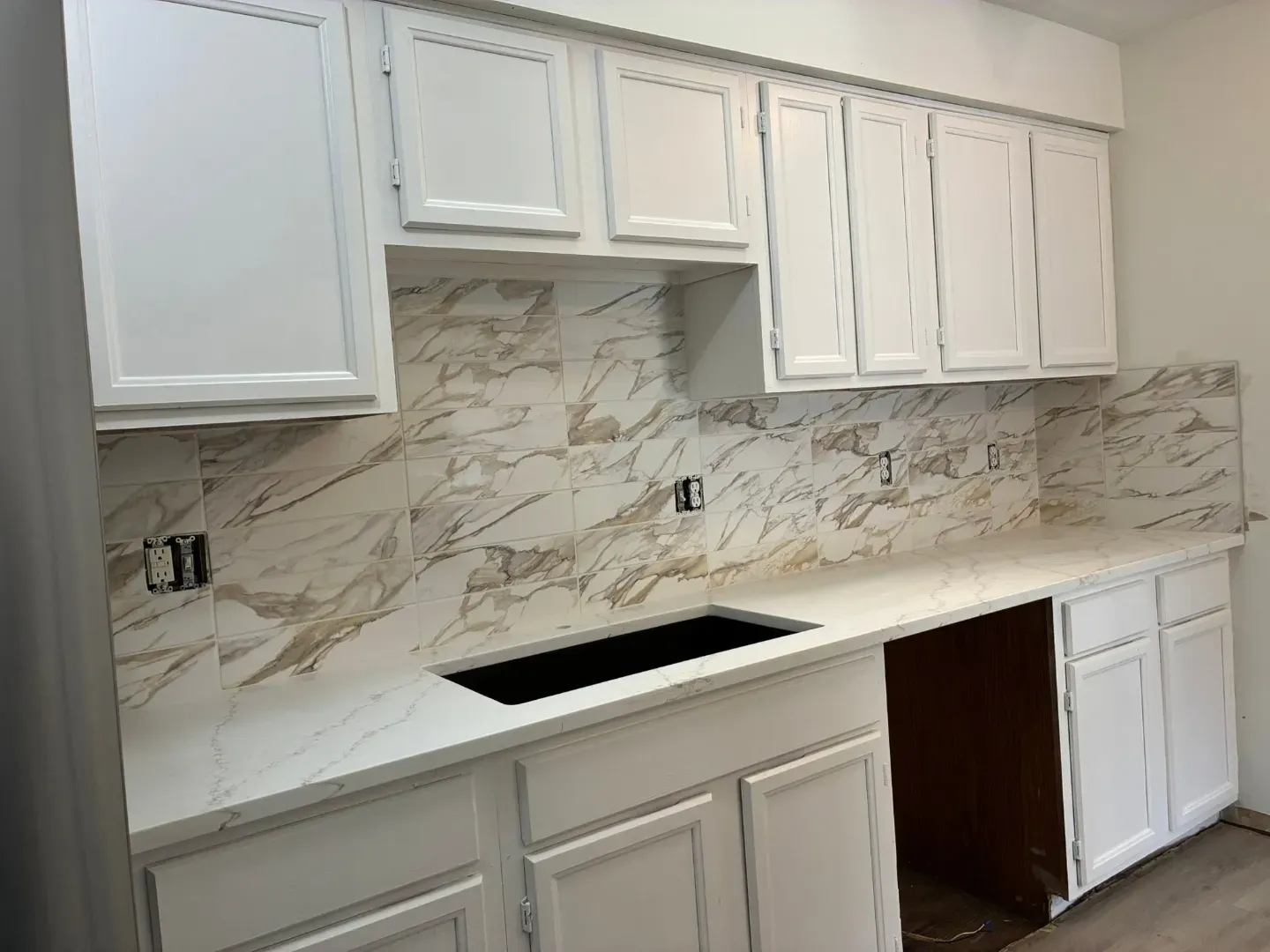 Kitchen run of white cabinets and a white counter with a tall marble-look slab backsplash with bold grey and gold veins